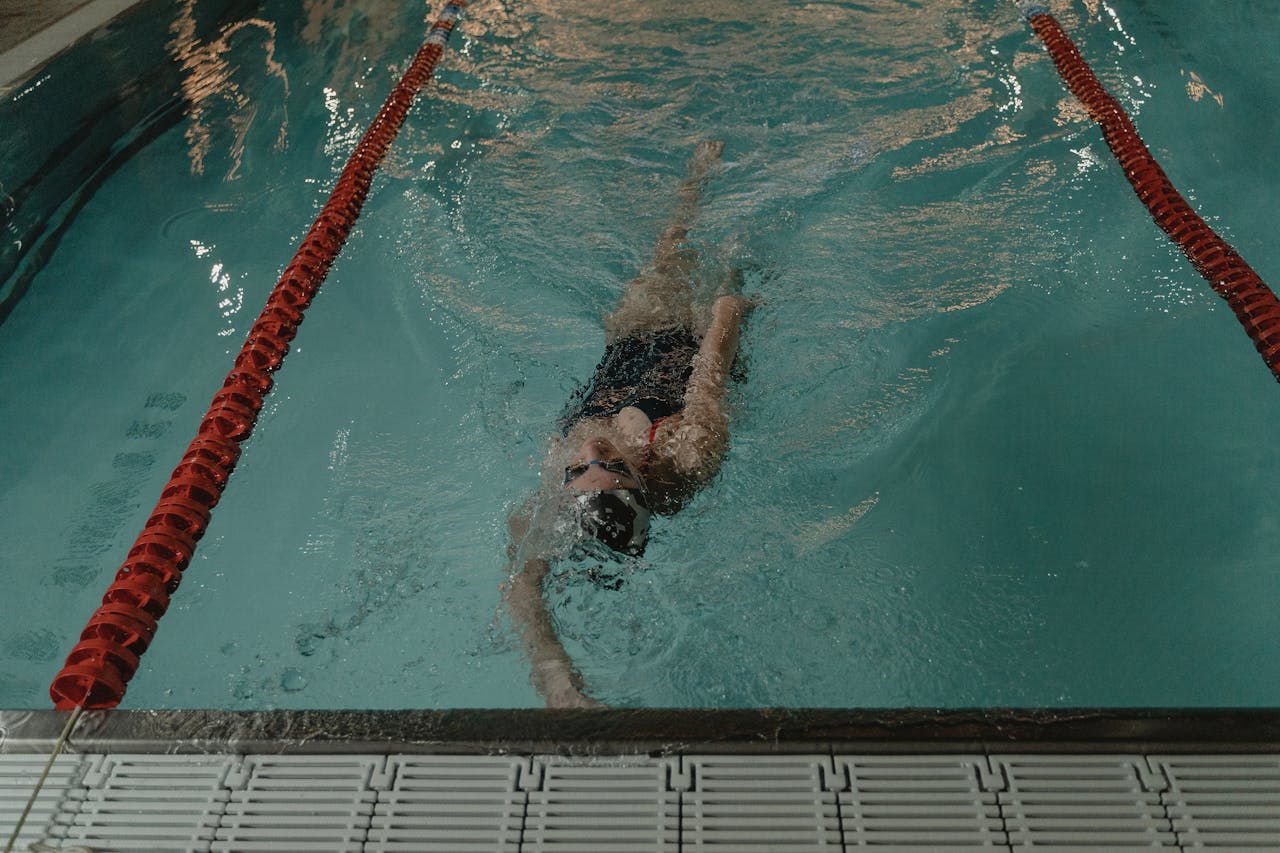 Swimmer performing backstroke in an indoor pool, showcasing professional swim technique.